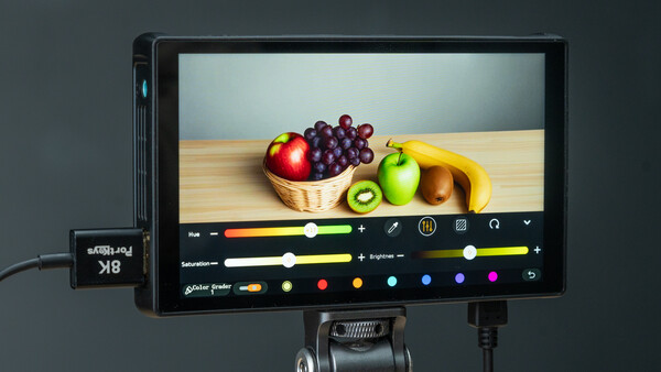 Professional monitor displaying fruit in a basket with color grading interface and control panel visible.