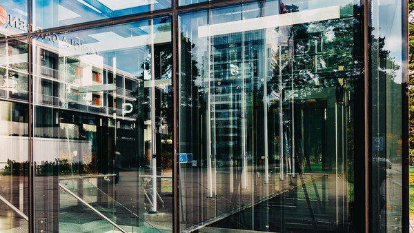 Modern glass storefront with reflections of surrounding buildings and trees on transparent panels.