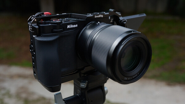 Nikon mirrorless camera with telephoto lens mounted on tripod against blurred outdoor background.