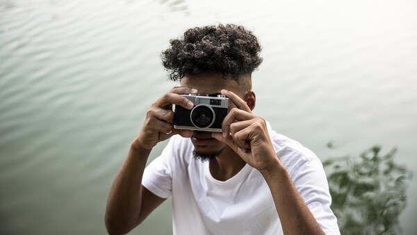 Person holding vintage rangefinder camera up to face by a body of water.