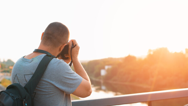 Photographer holding camera to face while standing on bridge at golden hour.