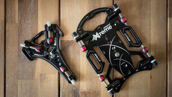 Two black mechanical disc brakes displayed on a wooden surface, showing different sizes and components.