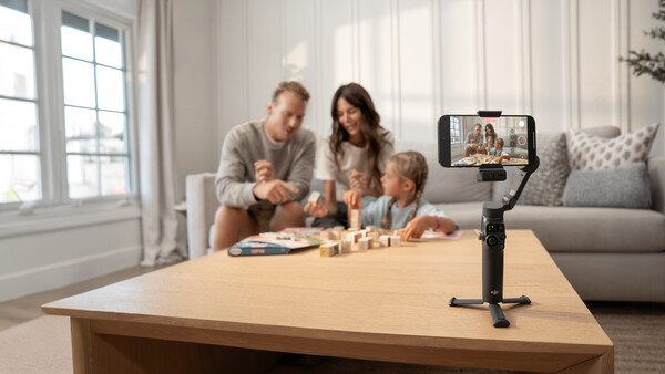 Smartphone mounted on tripod recording family playing board game at wooden table.