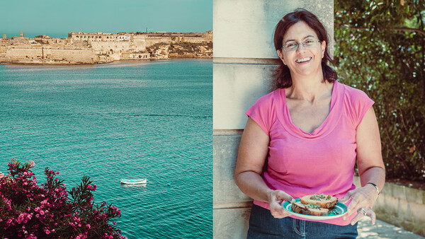 Woman in pink shirt holding colorful food beside Mediterranean coastal landscape.