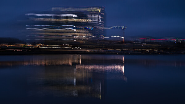 Modern building with illuminated windows reflected in still water at twilight.
