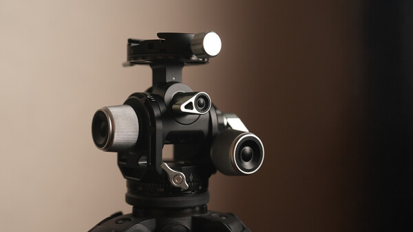 Professional cinema camera head with multiple lens ports and mounted LED light on tripod.