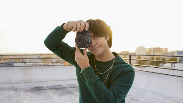 Photographer holding vintage film camera up to face on urban rooftop during golden hour.