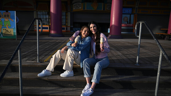 Three young people sitting together on a shaded platform with colorful building columns in background.