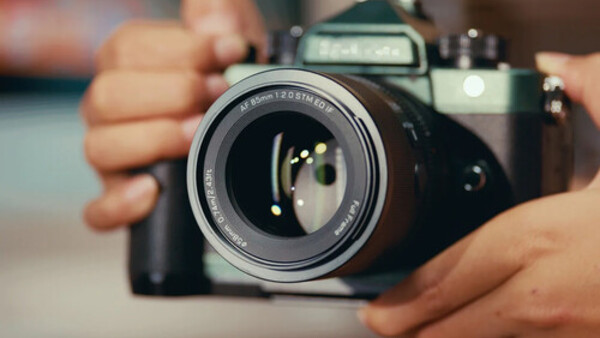 Photographer's hands holding a vintage SLR camera with lens extended, demonstrating proper grip and positioning.