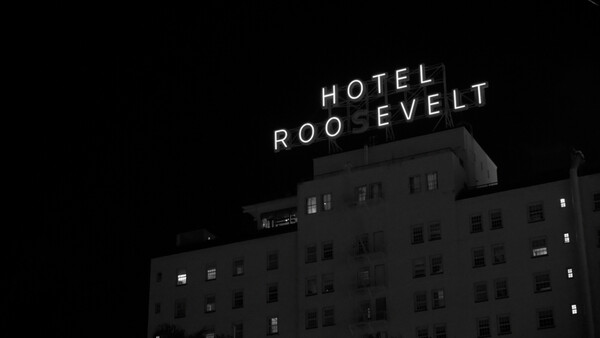 Hotel Roosevelt neon sign glowing on top of a dark multi-story building at night.