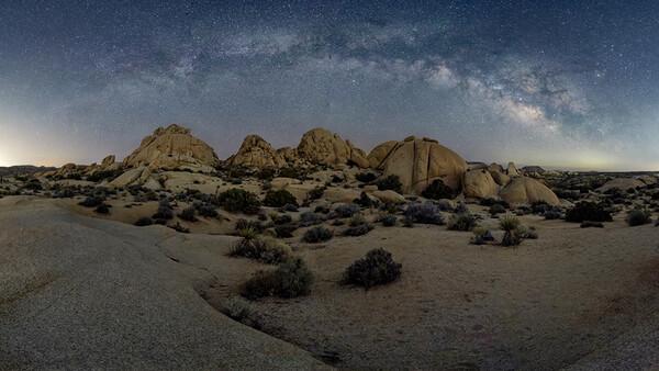 Desert landscape with large granite rock formations under a starry night sky with visible Milky Way.