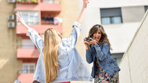 Photographer capturing a candid moment of a woman with raised arms making peace signs outdoors.