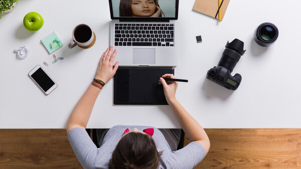 Overhead view of a creative professional's desk with laptop, graphics tablet, camera gear, and coffee.