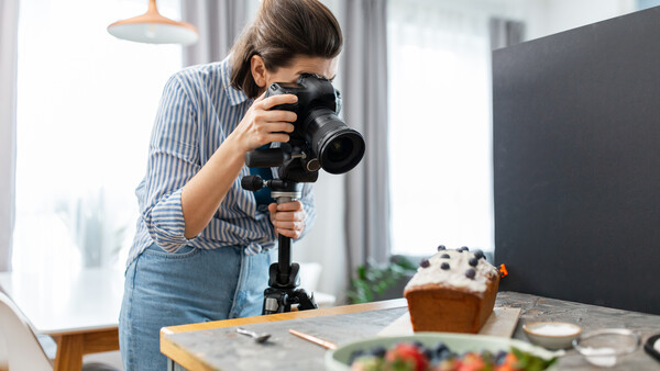 Food photographer shooting a styled flat lay setup with a DSLR camera on a tripod in a bright studio.