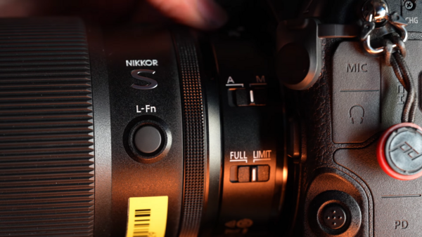 Nikon L-Fn lens with camera body and accessories in warm studio lighting.