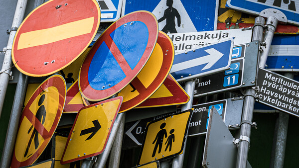 Stacked traffic signs with red no-entry circles and yellow warning signs featuring pedestrian symbols.