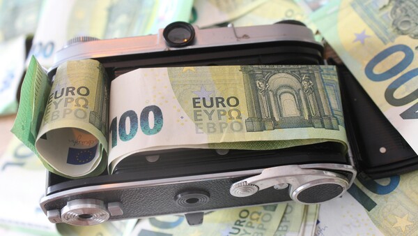 Vintage film camera wrapped in Euro banknotes, photographed on a surface covered with additional currency.