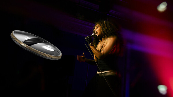 Singer performing at microphone with dramatic stage lighting and glowing circular light fixture.