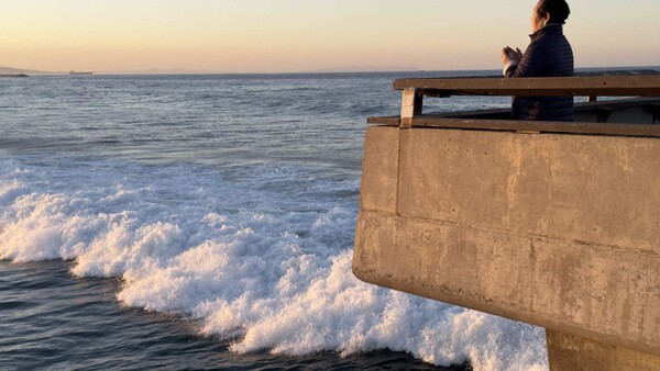 Person sitting on concrete pier overlooking ocean waves at dusk.