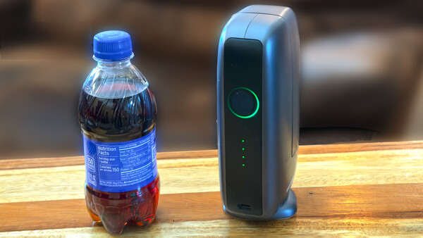 A dark carbonated beverage bottle and a portable wireless charging device positioned side by side on a wooden surface.