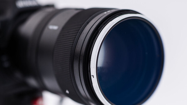 Close-up of a telephoto lens with a dark blue circular filter element and metallic focus ring against a white background.