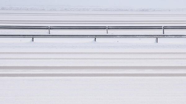 Aerial view of a snow-covered highway with guardrails and lane markings visible from above.