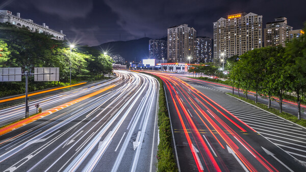 Long exposure photograph of highway traffic at night with light trails from vehicles streaming in multiple directions.