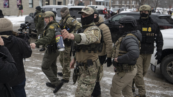 Armed personnel in tactical gear and winter clothing gathered in a snowy urban plaza during daytime.