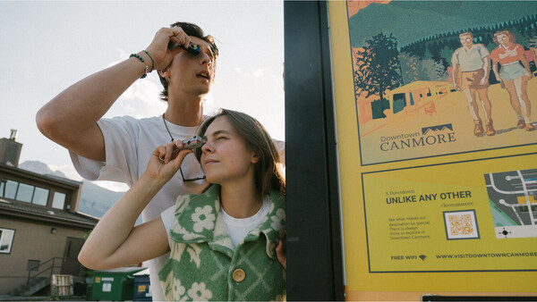 Two people sharing ice cream cones outdoors on a city street, with one person adjusting their sunglasses.