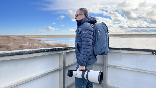 Birdwatcher with telephoto lens and backpack observing wetlands from an observation platform.