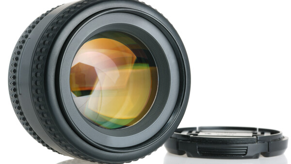Camera lens with amber-tinted glass elements and detached rear cap on white surface.