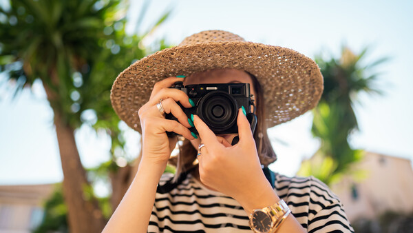 Photographer wearing a striped shirt and wide-brimmed straw hat holding a rangefinder camera up to their face.