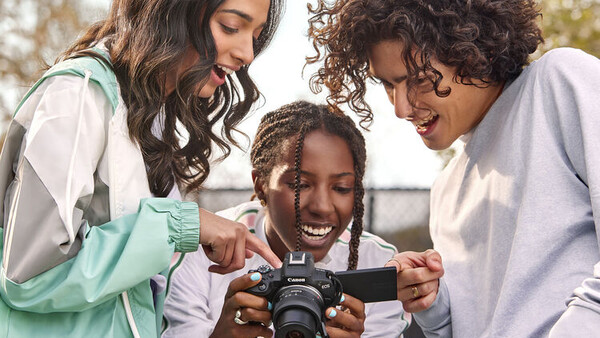 Three women smiling while looking at a camera display in outdoor daylight.