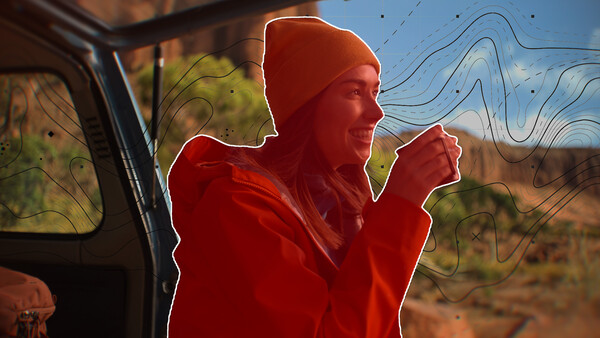 Person in red jacket and beanie leaning out of vehicle window against desert landscape.