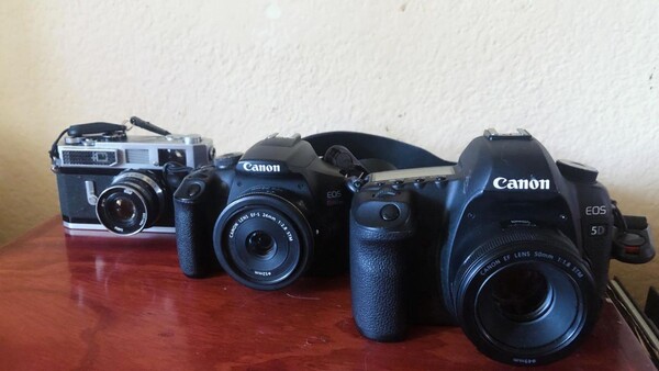 Three Canon cameras arranged in chronological order on a wooden surface, ranging from vintage rangefinder to modern DSLR.