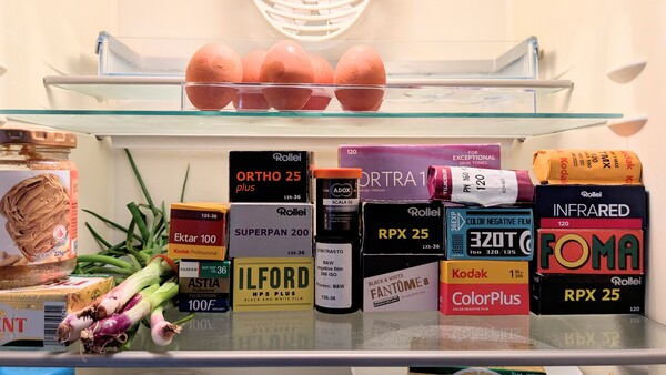 Refrigerator shelf displaying vintage film stock boxes and fresh produce including apples and vegetables.
