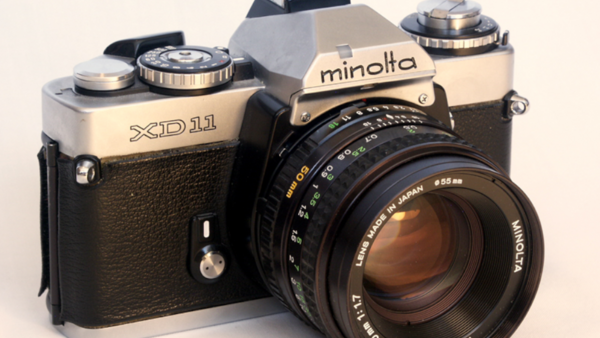 Minolta XD11 film SLR camera with black leather grip and attached prime lens.