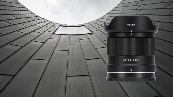 Viltrox AF 14/4.0 Z wide-angle lens with hood displayed against upward-angled architectural photograph of geometric building facade.