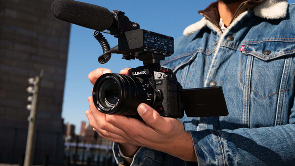 Videographer holding a cinema camera with an external monitor and microphone mounted on an urban rooftop.