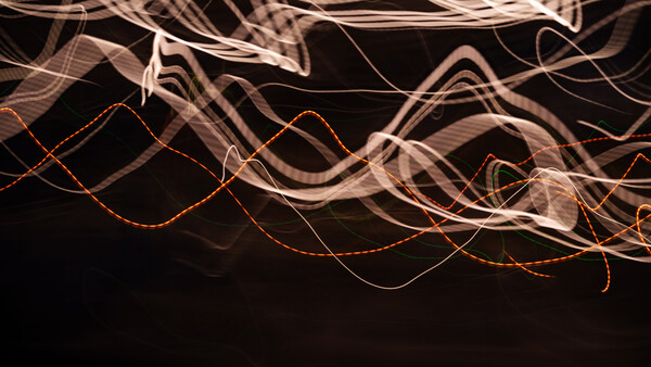 Light painting photograph with flowing curves of orange and white light trails against black background.