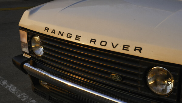 Classic Range Rover front end with cream-colored hood and black grille in daylight.