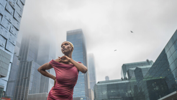 Woman in burgundy dress posing against urban skyline with tall buildings obscured by fog.