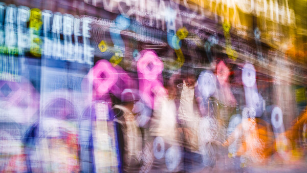 Blurred neon signs and pedestrians on an urban street at night, with magenta and blue glowing lights.