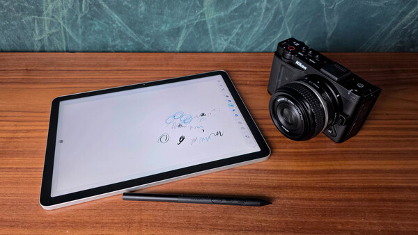 Digital tablet with stylus and vintage film camera on wooden desk.
