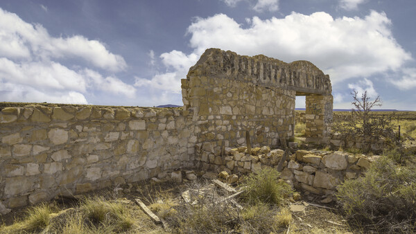 Ruined stone structure with rectangular opening in arid landscape under cloudy sky.