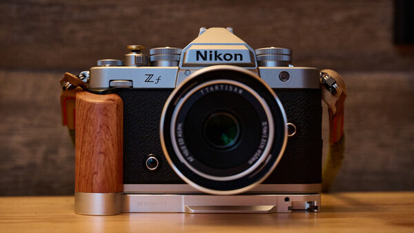 Nikon Z f mirrorless camera with wooden grip and attached lens, displayed on wooden surface.