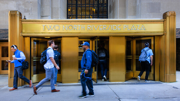 People in blue shirts entering a gold-framed entrance to Two North Riverside Plaza
