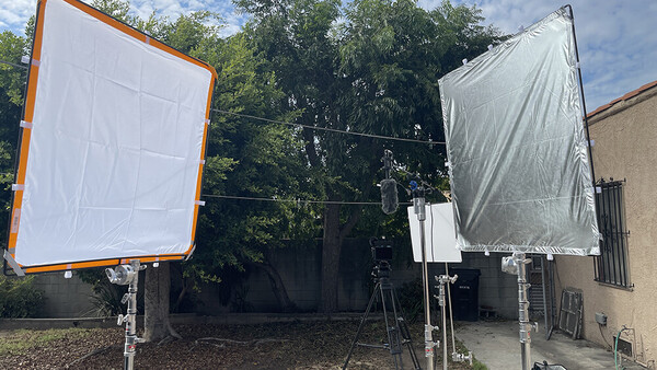 Two large fabric reflectors with orange and silver frames mounted on stands in a residential outdoor space