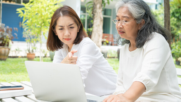 Two women in white shirts reviewing laptop screen outdoors in a garden setting.