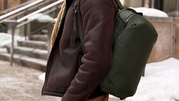 Person wearing a dark brown jacket and olive green backpack standing on outdoor steps.